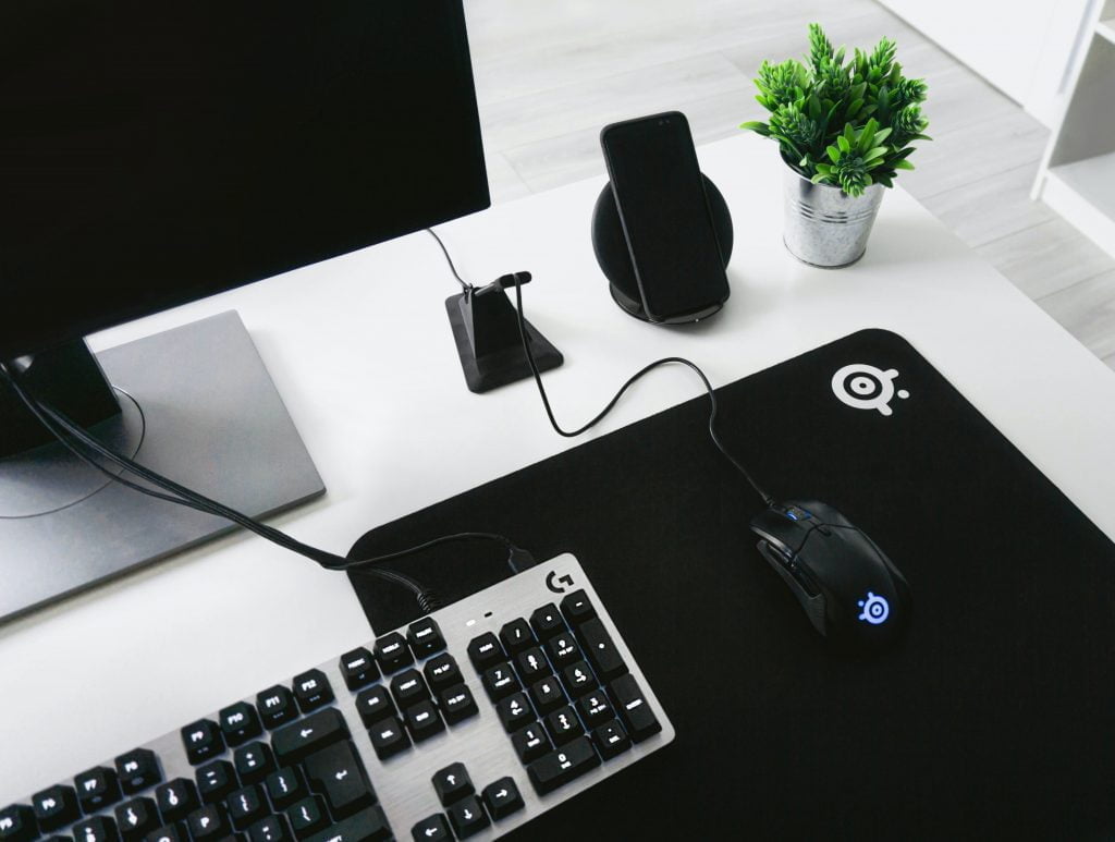 Computer, mouse, keyboard and phone on top of a sleek white desk.