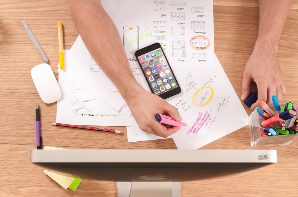 A desk with a person study notes from their phone and computer